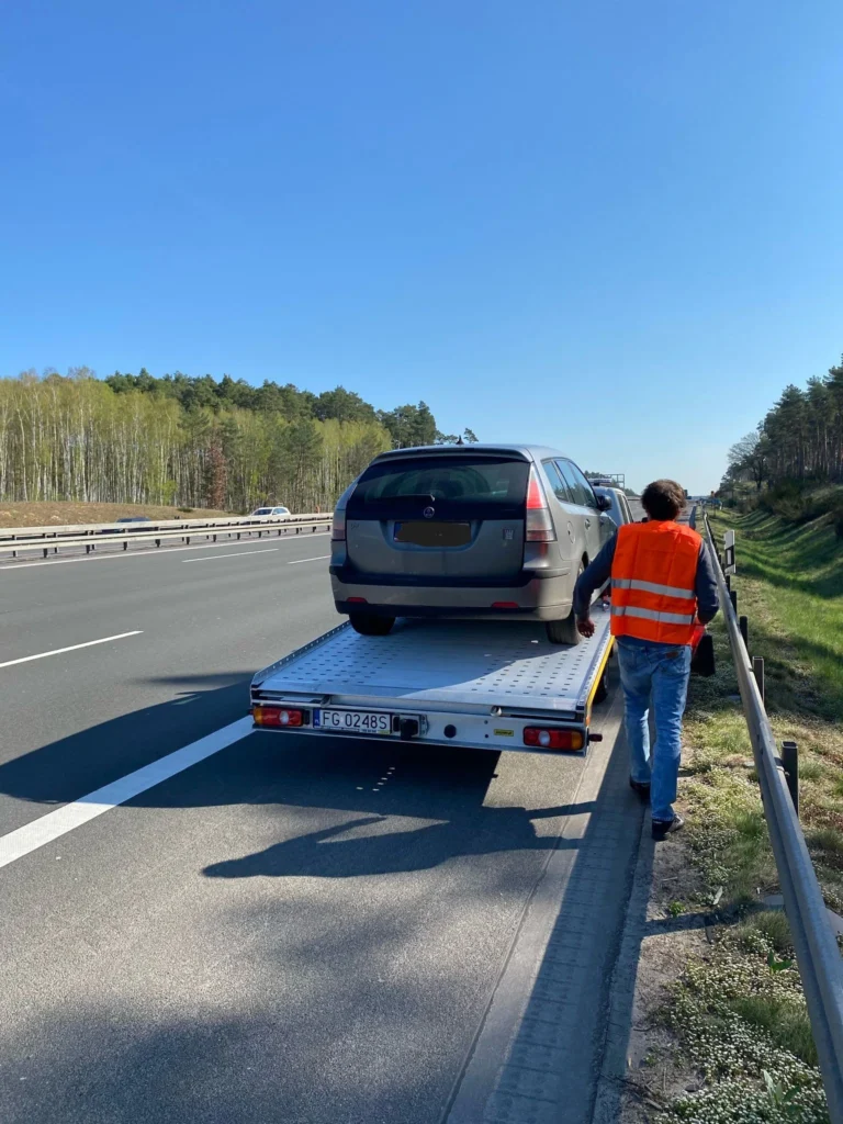 Samochód zatrzymany na poboczu, kierowca czeka na pomoc drogową Hannover, z widocznym trójkątem ostrzegawczym i wyposażeniem awaryjnym w tle